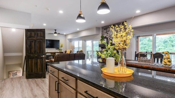 A modern kitchen with a marble countertop, dark cabinets, pendant lighting, and a view of the outdoors.