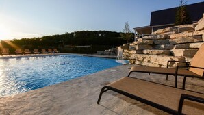 A swimming pool with lounge chairs, a stone wall, and a building in the background.