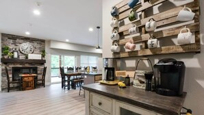 A modern kitchen with a stone fireplace, wooden wall decor, and a coffee station.