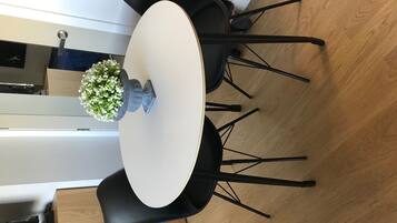 Una mesa redonda con cubierta blanca, rodeada de sillas negras. Hay una pequeña maceta con flores blancas sobre la mesa.