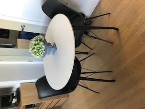 Una mesa redonda con cubierta blanca, rodeada de sillas negras. Hay una pequeña maceta con flores blancas sobre la mesa.