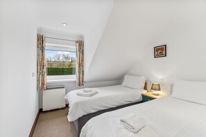 A room with two beds, a window with curtains, a picture on the wall, and a bedside lamp.