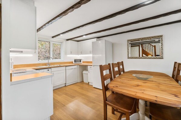 A modern kitchen with white appliances, wooden flooring, and exposed beams on the ceiling. - Conveniently located to explore all that Cornwall and Devon have to offer (Notter Bridge)