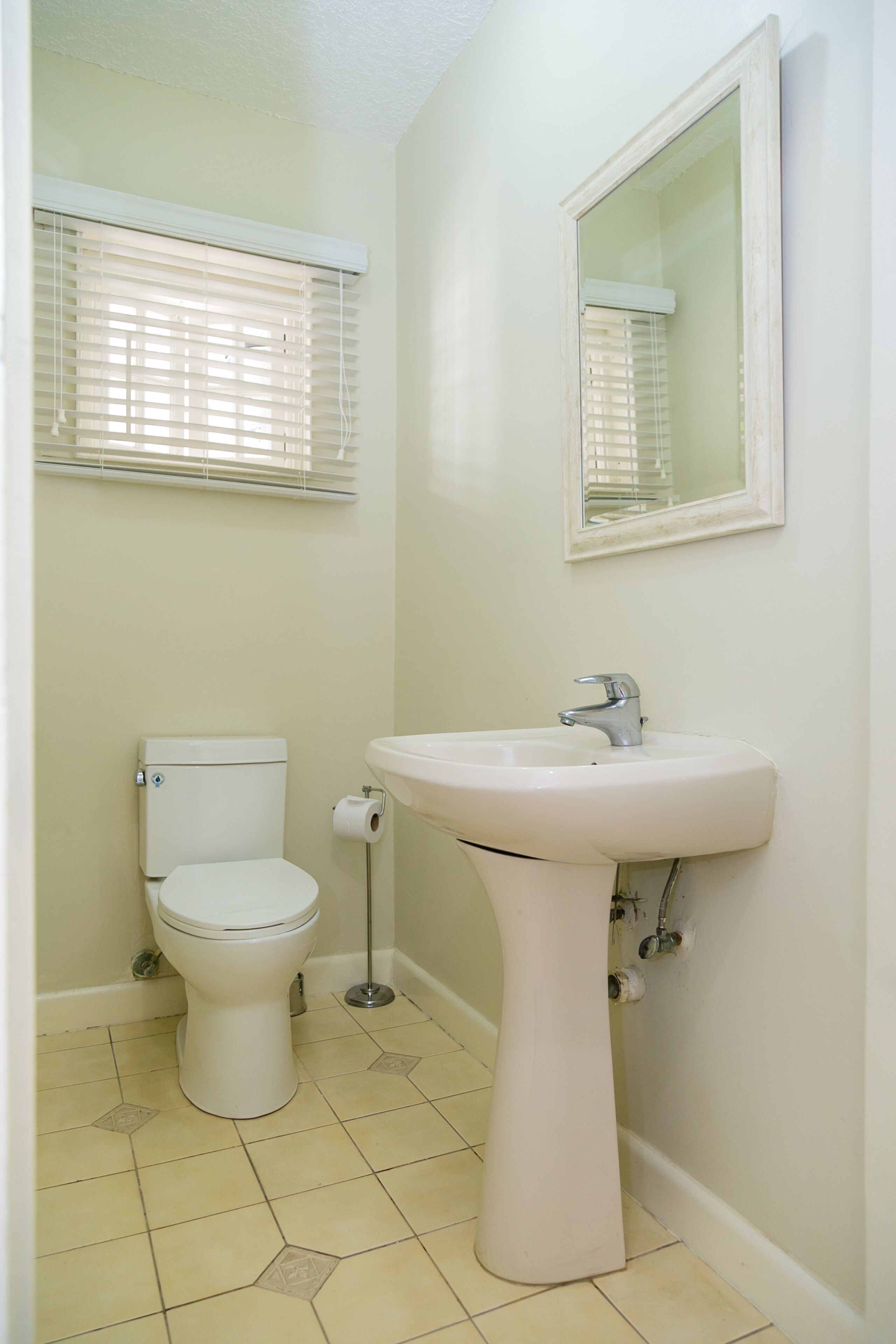 Un baño con inodoro, lavamanos y ventana con persianas.