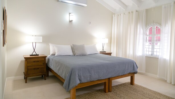 Une chambre à coucher avec un lit en bois, deux tables de chevet avec des lampes, un climatiseur et une fenêtre avec des rideaux.