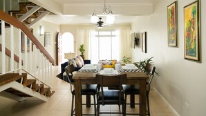 Un coin repas avec une table en bois dressée pour quatre personnes, un escalier avec des rampes blanches et deux tableaux encadrés accrochés au mur.