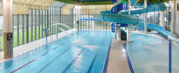 Une piscine intérieure dotée de plusieurs couloirs, d’un toboggan aquatique et d’un espace clos par des parois de verre.