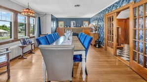 A dining area with a long table, blue upholstered chairs, and a chandelier. - Nicklin House (Leamington)