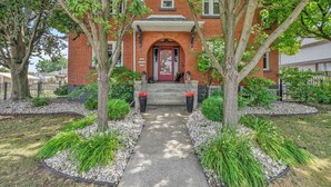 A brick building with a red door, surrounded by trees and a gravel pathway. - Nicklin House (Leamington)