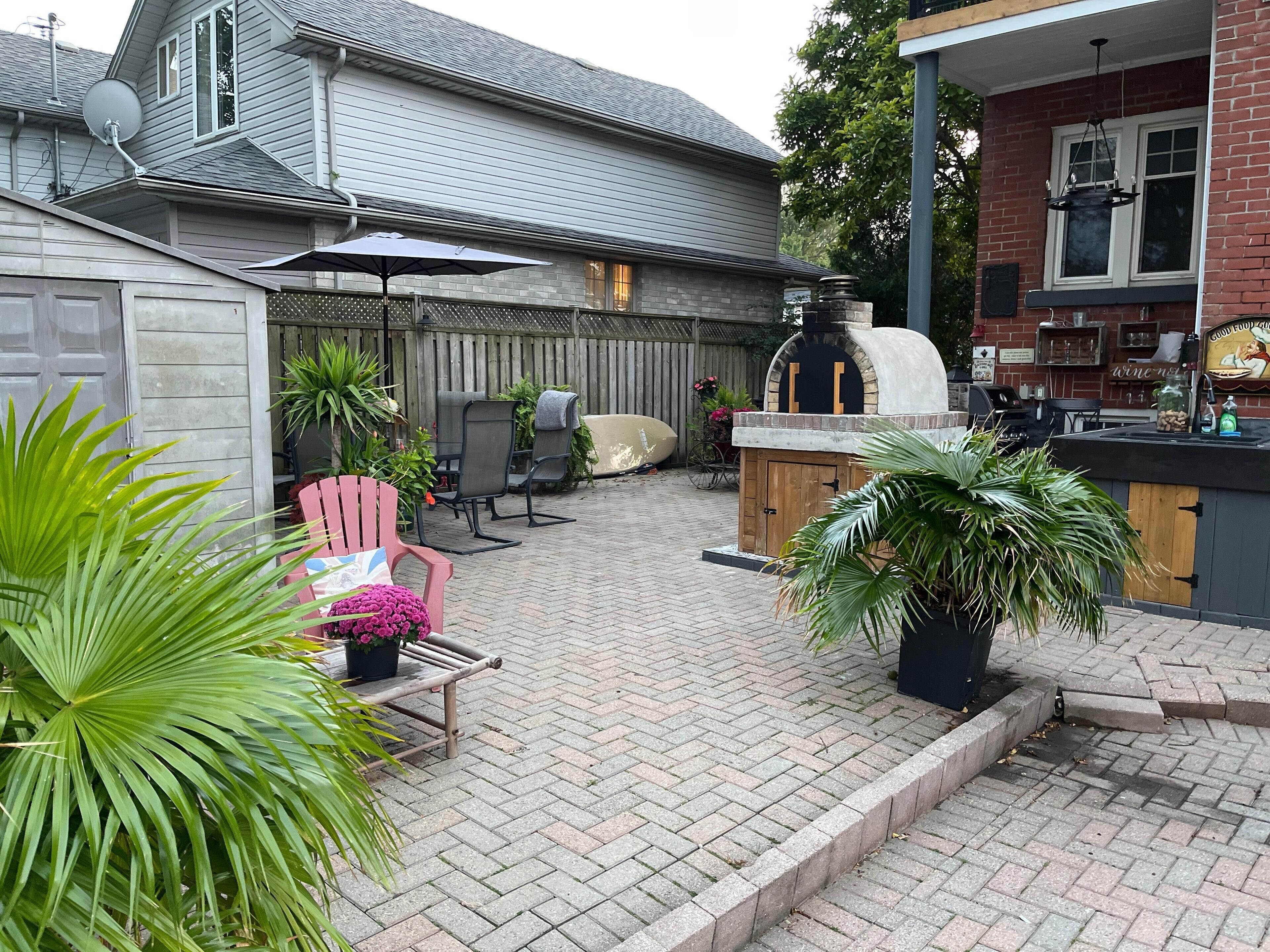 Une terrasse à l’arrière de la maison, avec un espace barbecue, des sièges d’extérieur et un chemin en briques.