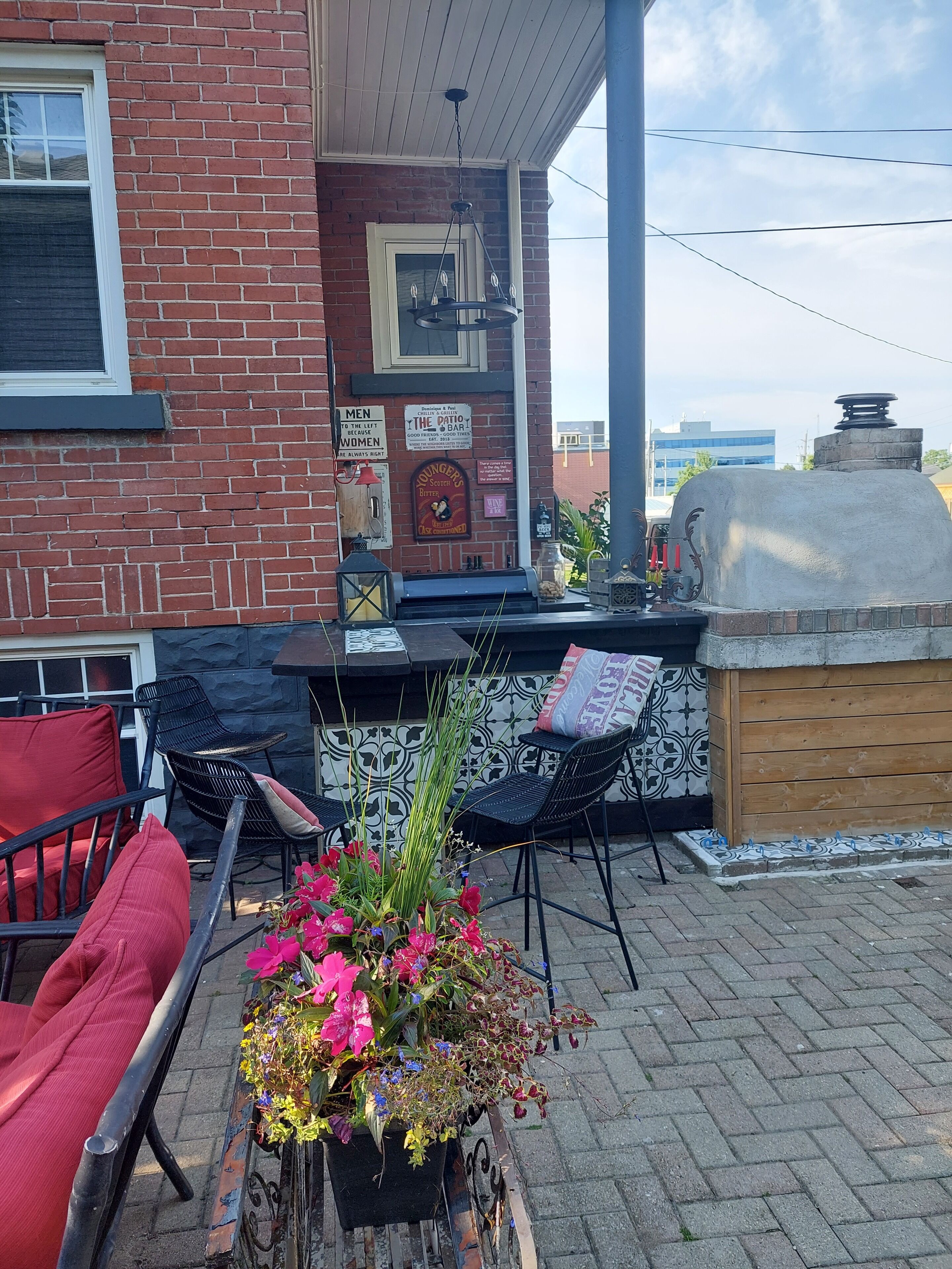 An outdoor patio area with brick walls, a grill, outdoor seating with chairs, and a flower arrangement.
