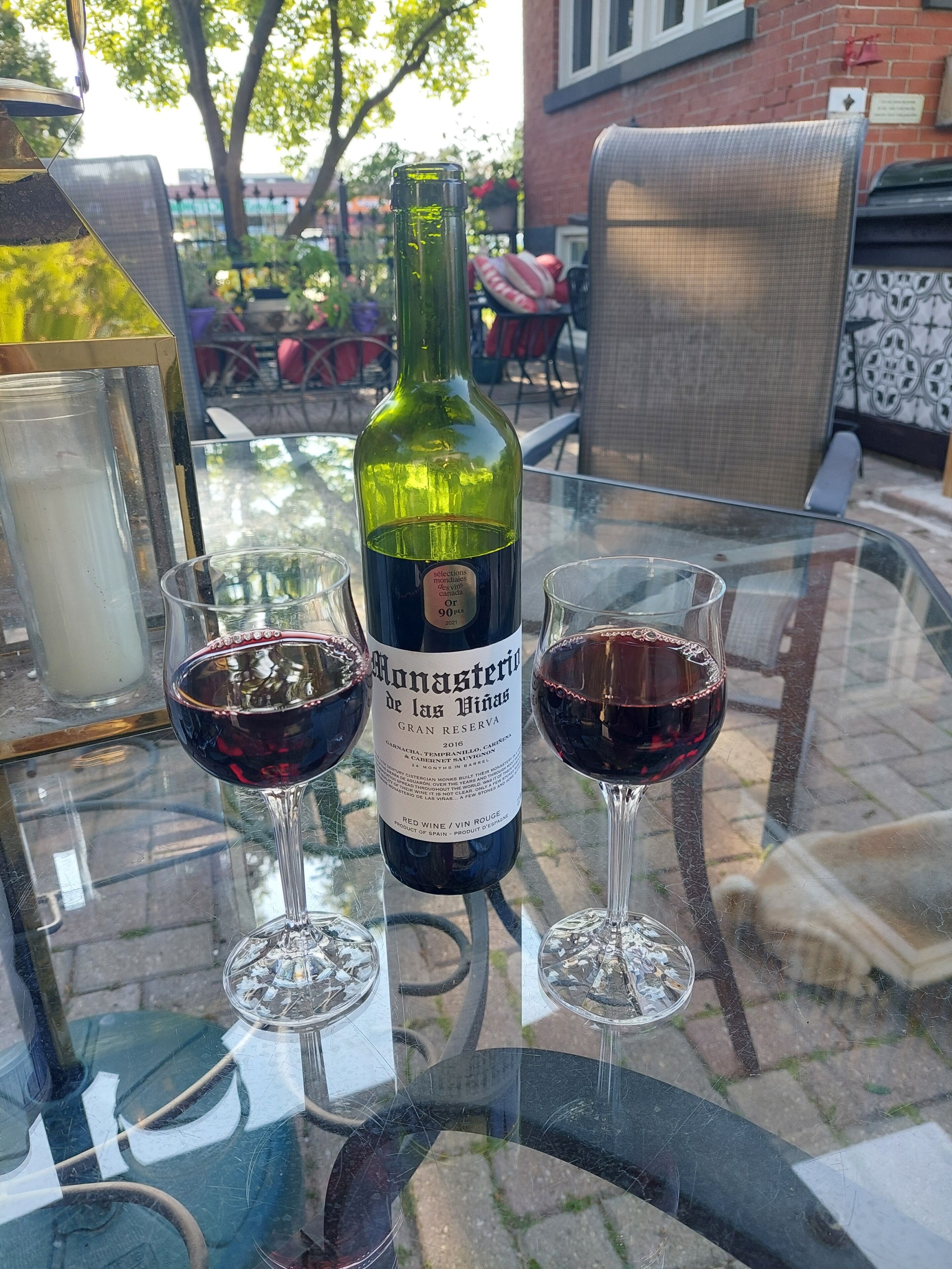 En flaska Monasterio de las Vinas Gran Reserva-vin står på ett glasbord, och bredvid finns två vinglas fyllda med rött vin.