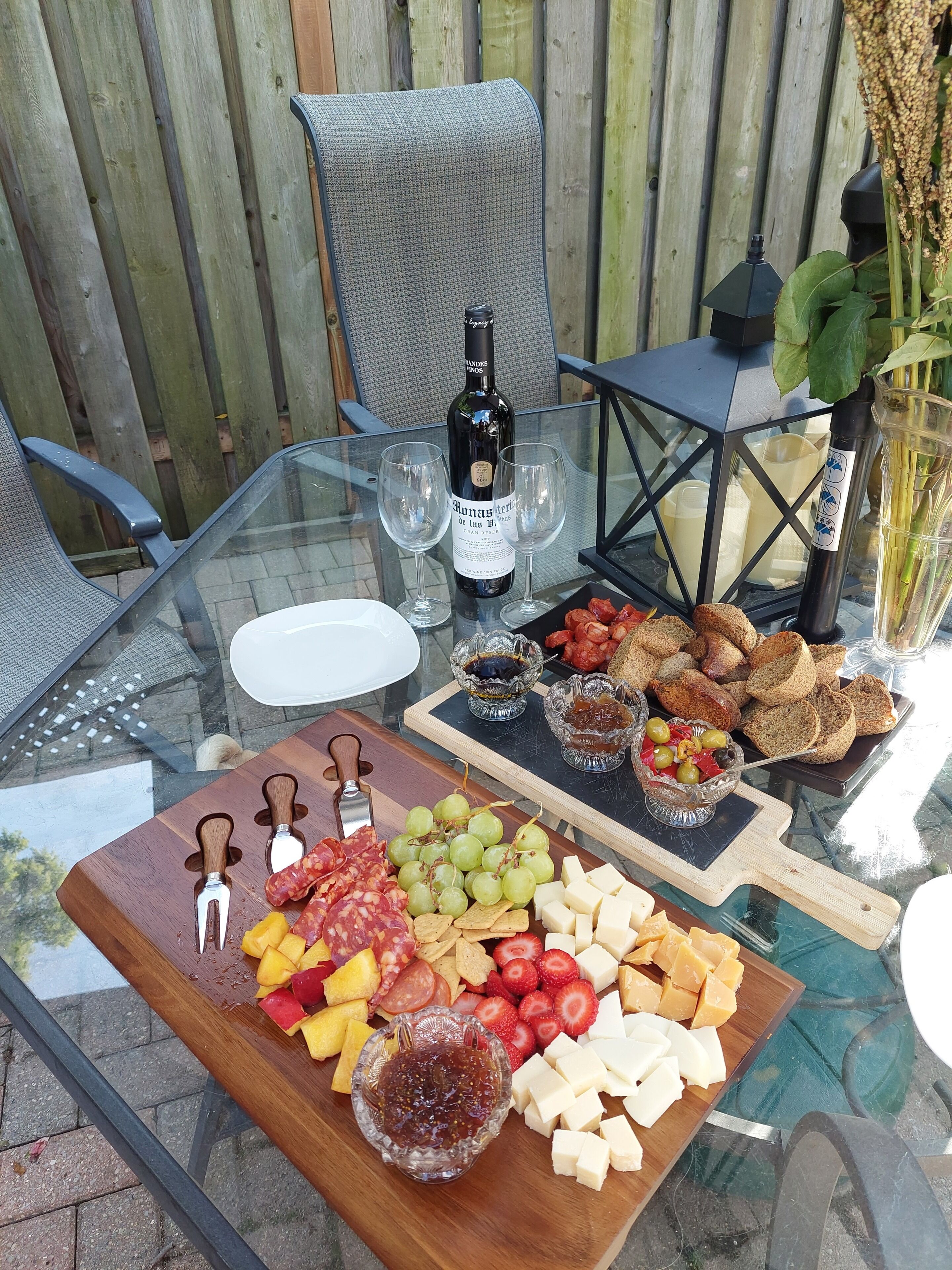 Ett bord med glasskiva, en vinflaska, två vinglas samt ett urval av snacks och frukter.