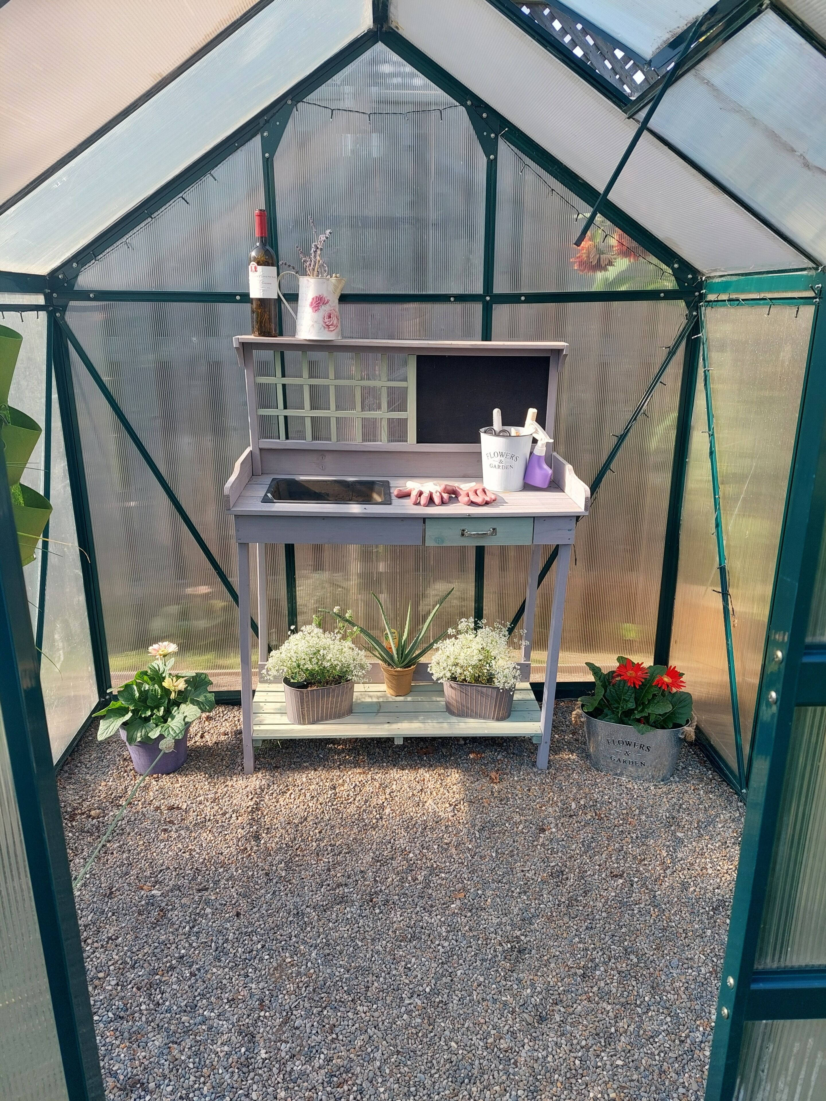 Une serre équipée d’un établi, de plantes en pot et d’une bouteille de vin.