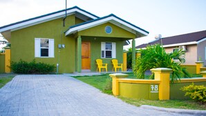 A two-story house with a paved driveway, a front porch with two yellow chairs, and a small garden area. - Drax Hall Manor Country Club Studio (Ocho Rios)
