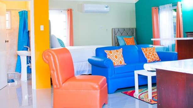 A modern living room with a blue sofa, orange armchair, and a white coffee table. - Drax Hall Manor Country Club Studio (Ocho Rios)