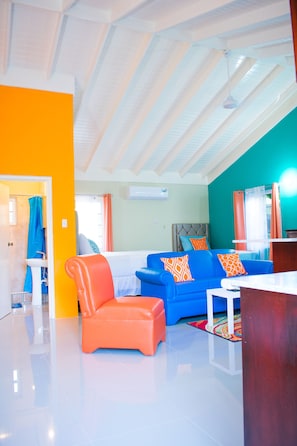 A modern living room with a blue sofa, orange armchair, and a white coffee table. - Drax Hall Manor Country Club Studio (Ocho Rios)