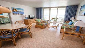 Een ruime woonkamer met rieten meubels, een eettafel en uitzicht op de zee door grote ramen.
