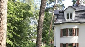A residential area with a white house featuring a small balcony, surrounded by trees and a paved road. - Villa Waldglück near Rangsdorfer See (Rangsdorf)