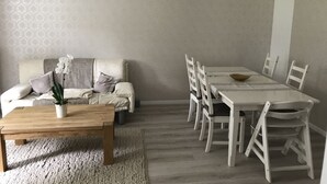 A dining area with a wooden table and white chairs, a sofa with cushions, and a potted orchid. - Villa Waldglück near Rangsdorfer See (Rangsdorf)