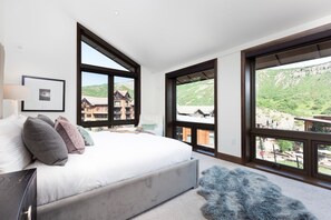 A bedroom with a large bed, multiple windows, and a view of a mountainous landscape.