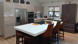 Una cocina moderna con una isla central, electrodomésticos de acero inoxidable y una zona de comedor con sillas de mimbre.