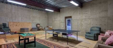 A room with a ping pong table, pool table, and comfortable seating.