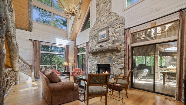 A spacious living room with a stone fireplace, wooden furniture, and large windows offering views of the outdoors.