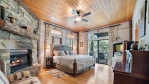 A cozy bedroom with a stone fireplace, a large bed, and a television.