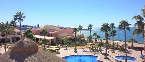 Zona de piscina en un resort con múltiples piscinas, palmeras y vista al océano.