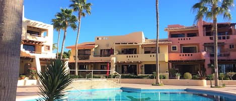 A pool area with palm trees, a building with balconies, and a clear blue sky.
