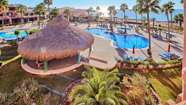 Un resort con varias piscinas, palmeras y una estructura con techo de paja.
