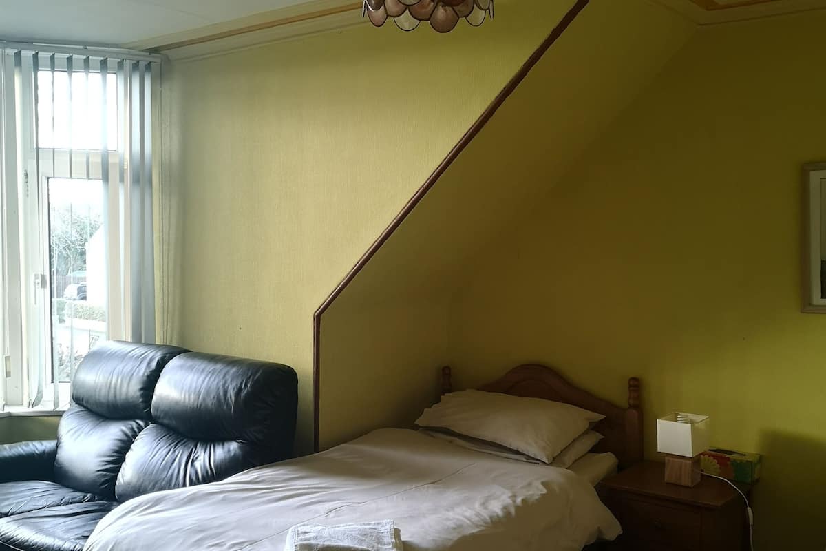 A bedroom with a bed, a nightstand, a lamp, a chair, and a window with blinds.