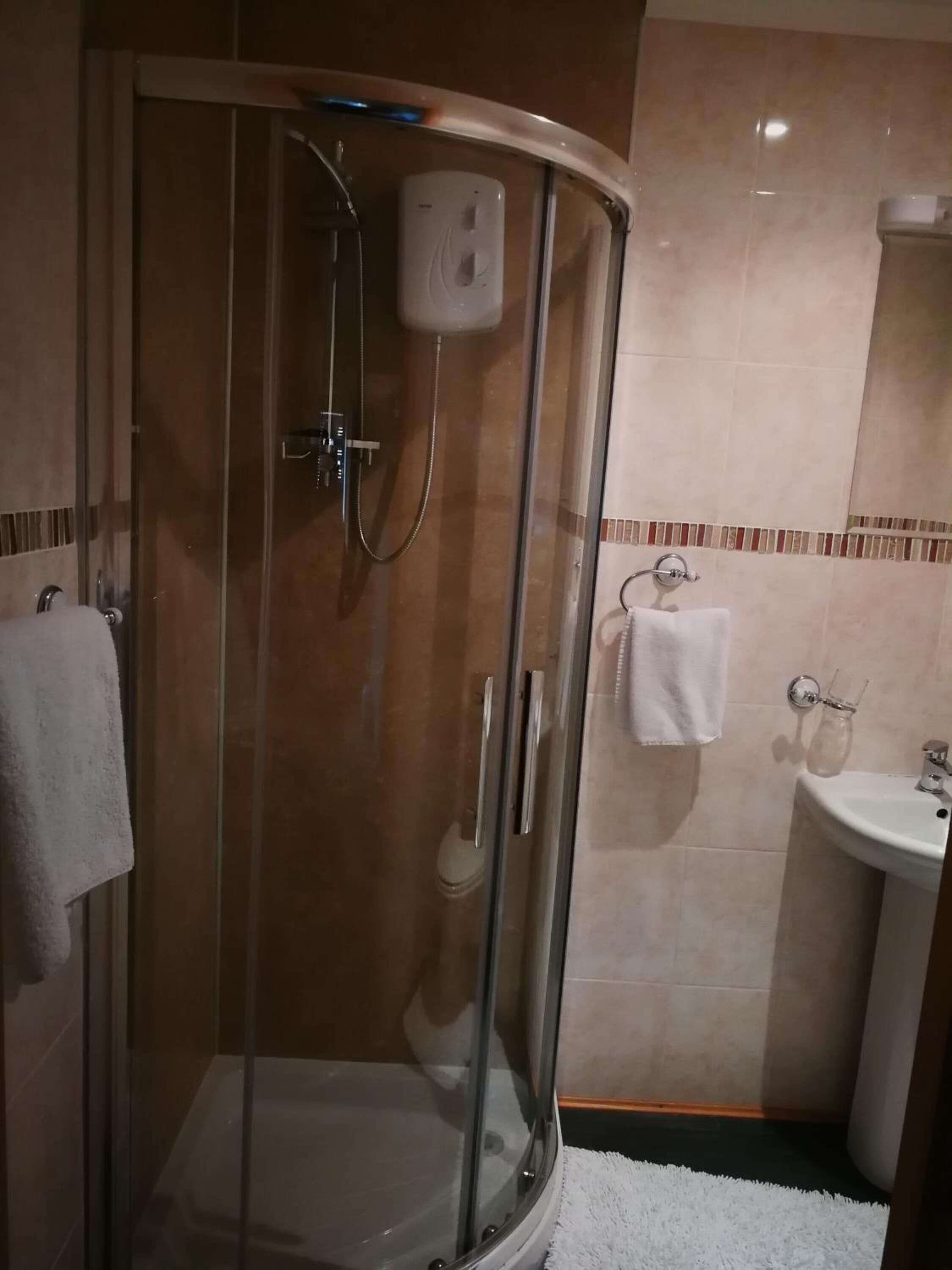 A glass-enclosed shower with a handheld showerhead, a white towel on the wall, and a sink with a glass jar.