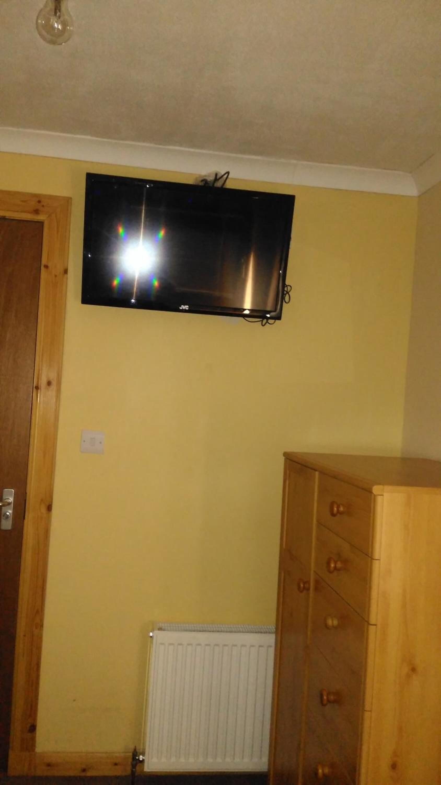 A room with a mounted flat-screen TV, a wooden cabinet, and a radiator.