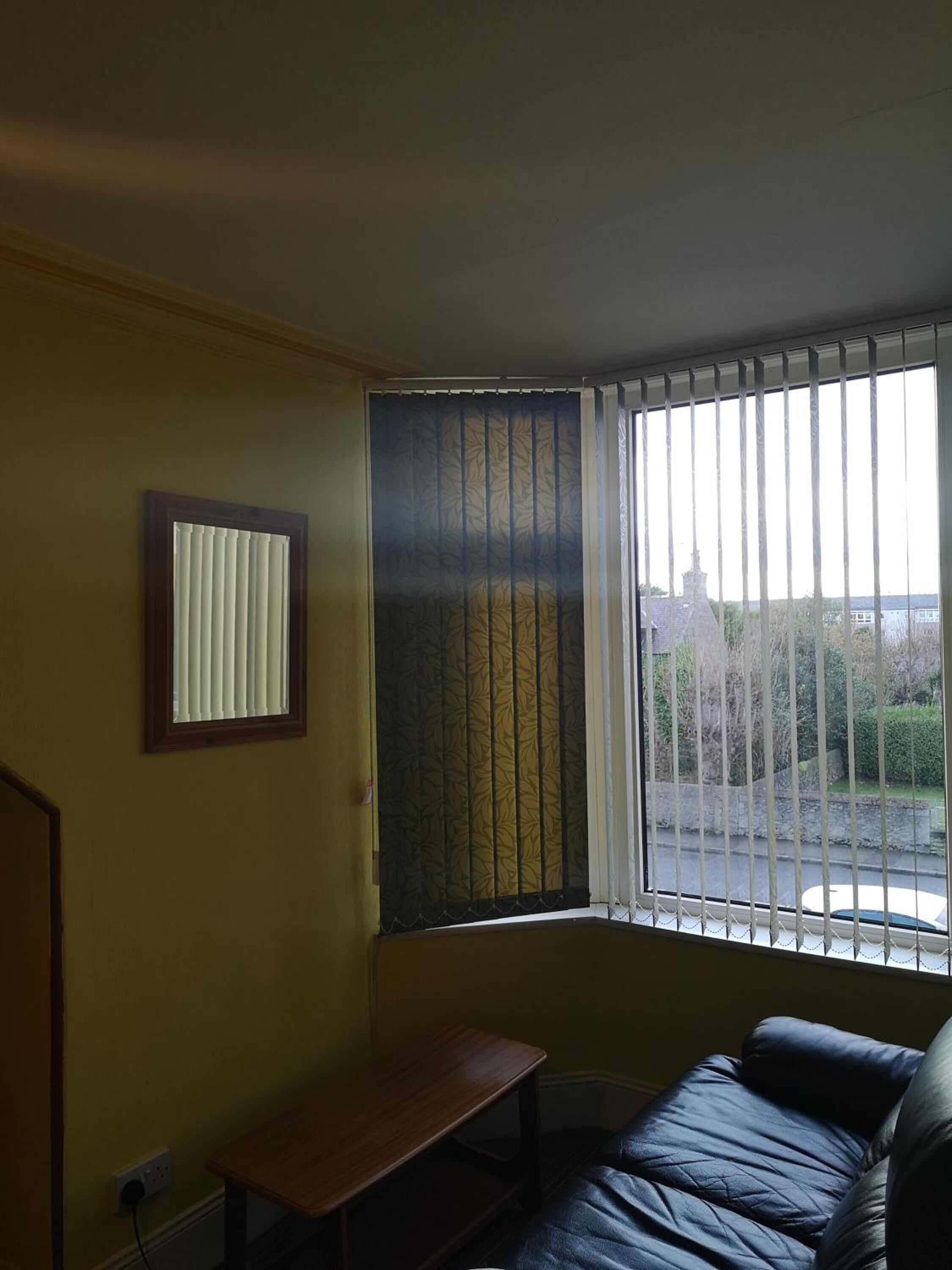 A room with a window, a sofa, a small table, and a wall-mounted light switch.