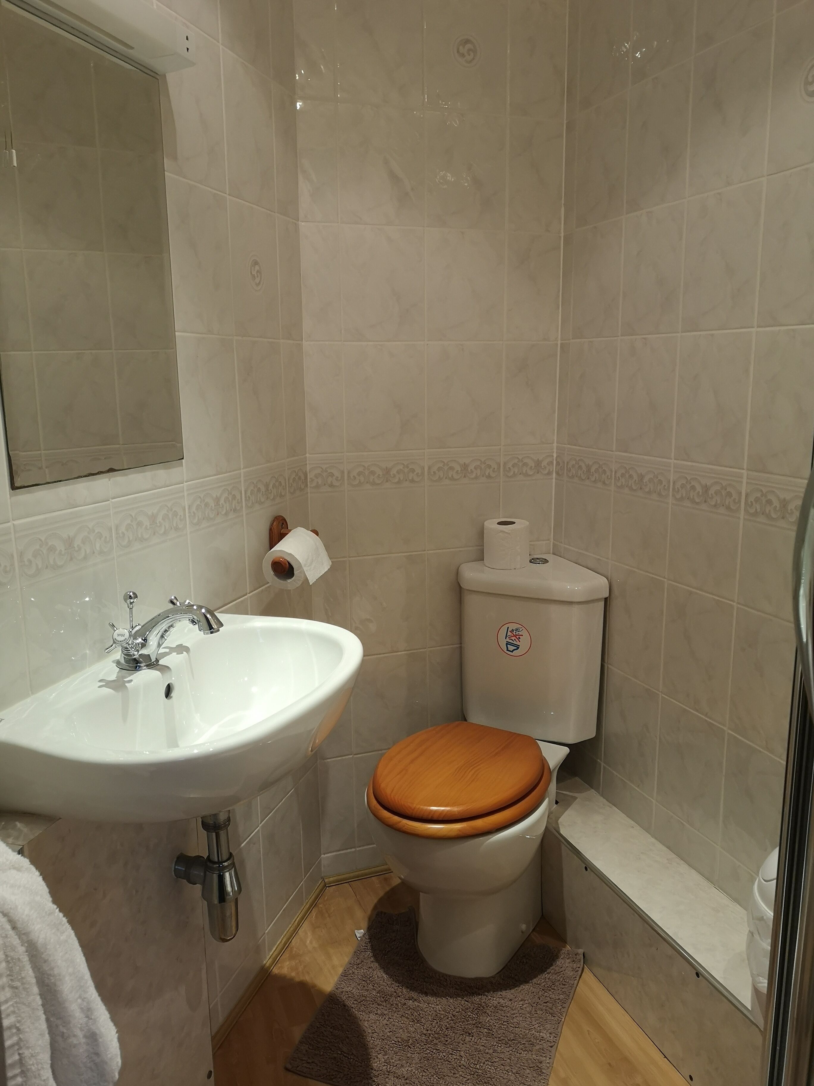 A bathroom with a white sink, a wooden toilet seat, and a toilet paper holder.
