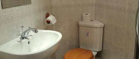 A bathroom with a white sink, a wooden toilet seat, and a toilet paper holder.