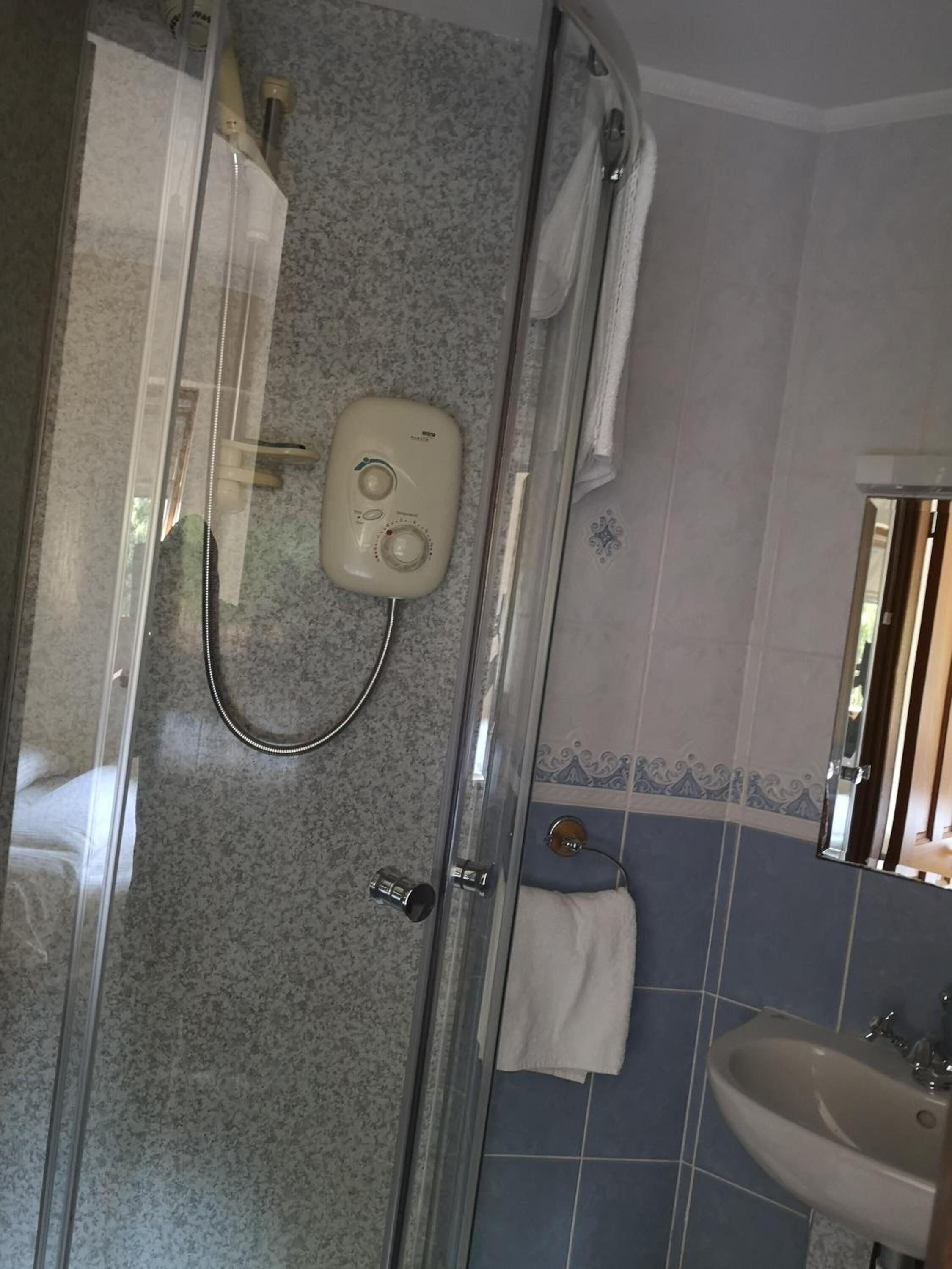 Ein Badezimmer mit Duschkabine aus Glas, einem weißen Handtuch an der Wand und einem Waschbecken mit Spiegel.