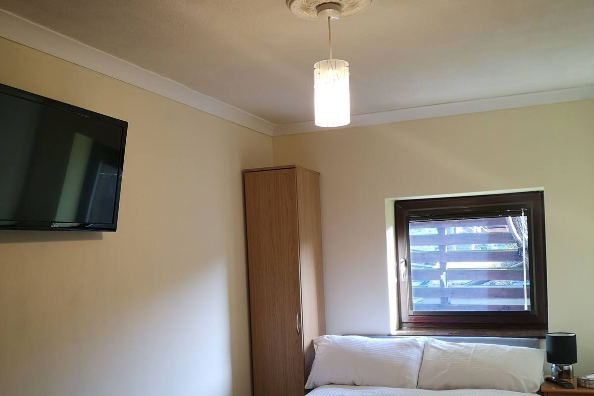 A bedroom with a bed, a wardrobe, a radiator, a TV mounted on the wall, and a window with blinds.