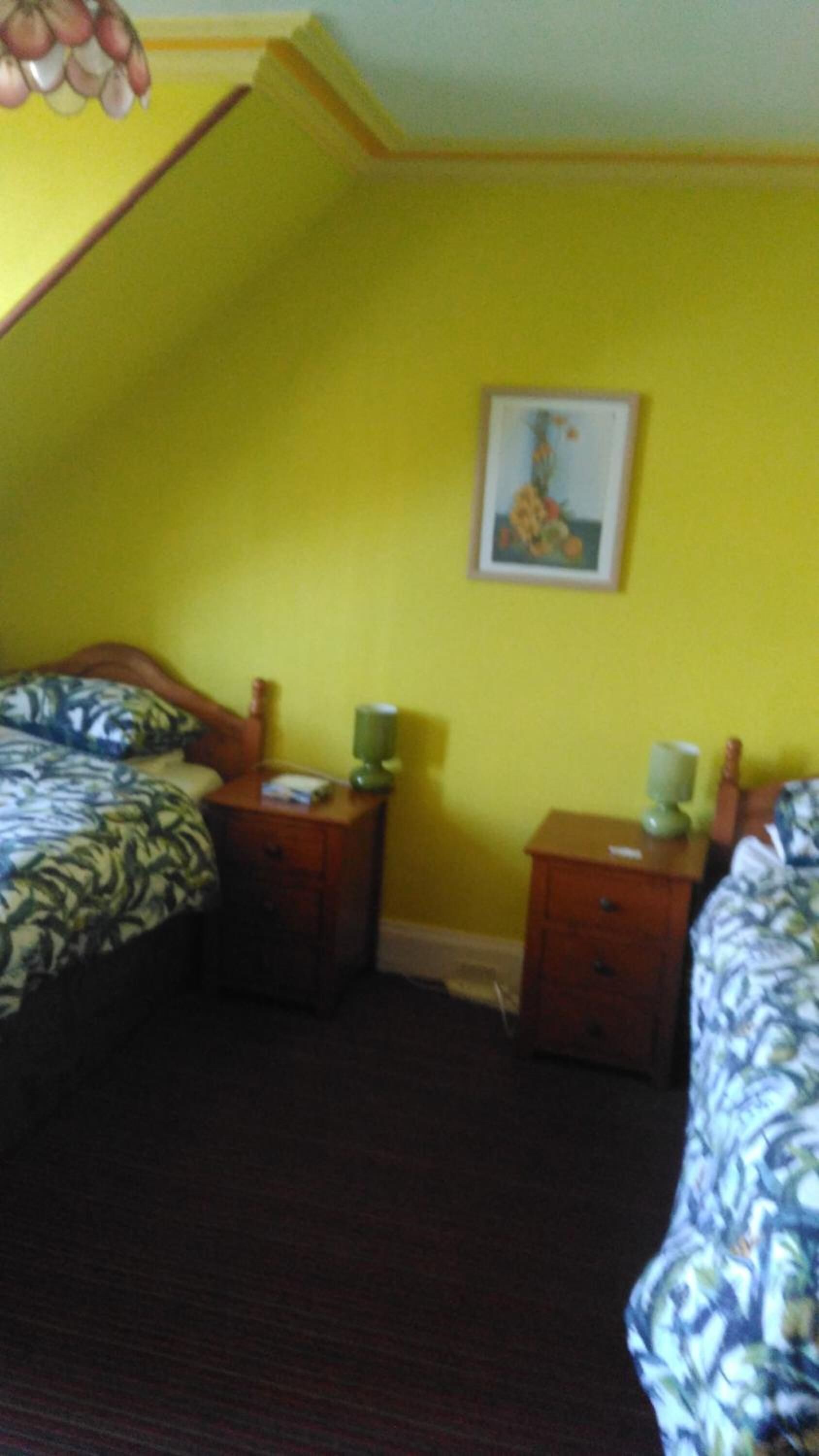 A room with two beds, a small table, a nightstand, and a wall-mounted picture.