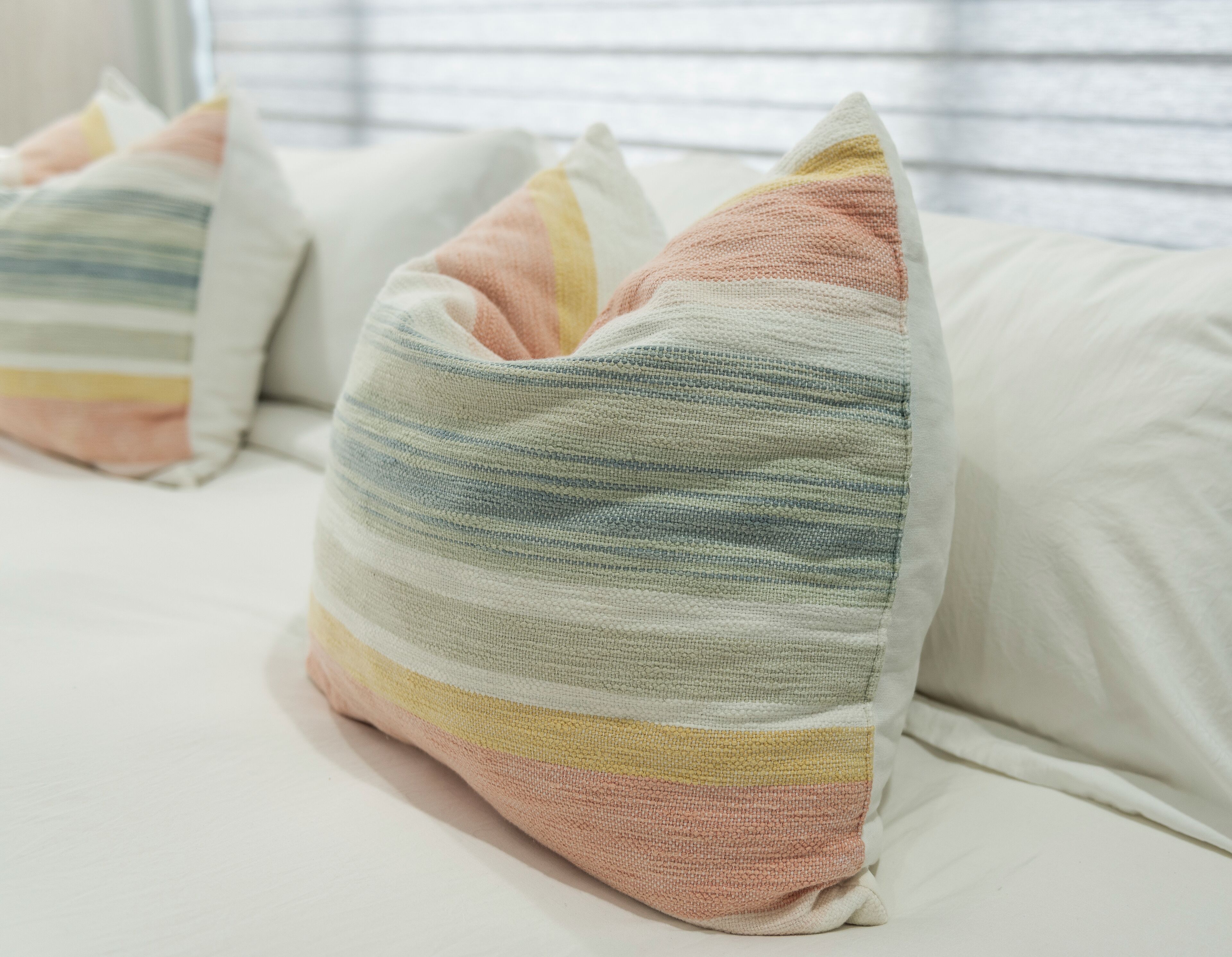 A bed with white bedding and striped pillows in pastel colors.