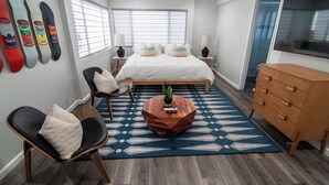 A bedroom with a bed, bedside tables, a TV, a wooden dresser, a chair, a coffee table, and a wall with skateboard art. - Belmont Shore Peninsula - 2 King Suites 2.5Baths - Roof Deck + Garage - Sleeps 6 (Long Beach)