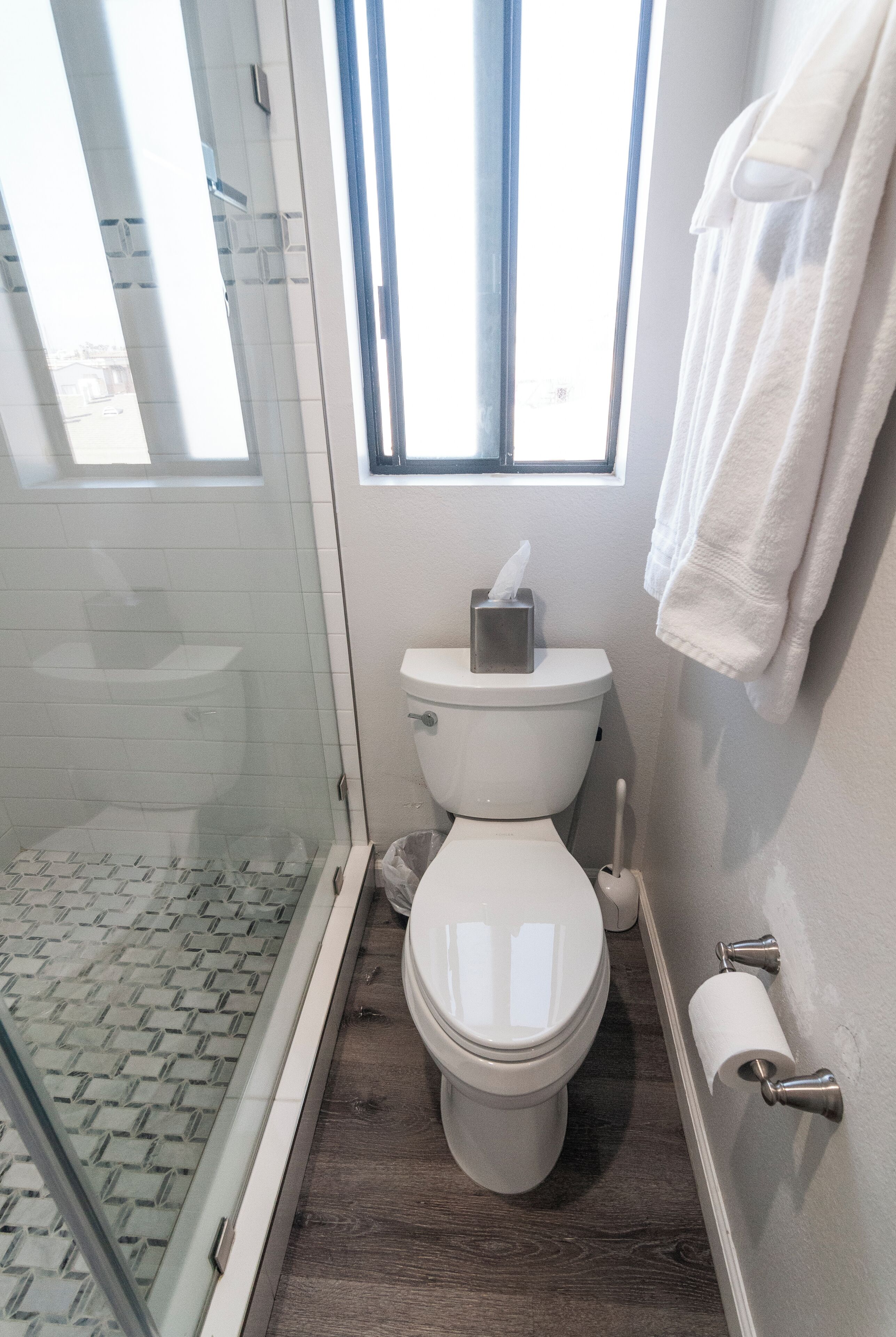 A modern bathroom with a glass shower enclosure, a toilet, and a window providing natural light.