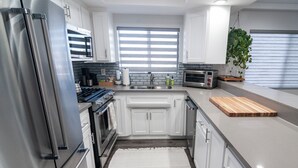 A modern kitchen with white cabinets, stainless steel appliances, a wooden cutting board, and a potted plant. - Belmont Shore Peninsula - 2 King Suites 2.5Baths - Roof Deck + Garage - Sleeps 6 (Long Beach)