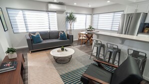 A modern living room with a grey sofa, a coffee table, and a dining area with chairs and a small table. - Belmont Shore Peninsula - 2 King Suites 2.5Baths - Roof Deck + Garage - Sleeps 6 (Long Beach)