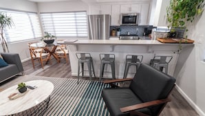 A modern kitchen with stainless steel appliances, a bar area with stools, and a dining table with chairs. - Belmont Shore Peninsula - 2 King Suites 2.5Baths - Roof Deck + Garage - Sleeps 6 (Long Beach)