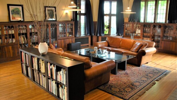 A spacious living room with a leather sofa, a coffee table, and a bookshelf filled with books. - Architect's Brownstone Mansion 6B6B, Porch, Garden (Minneapolis)