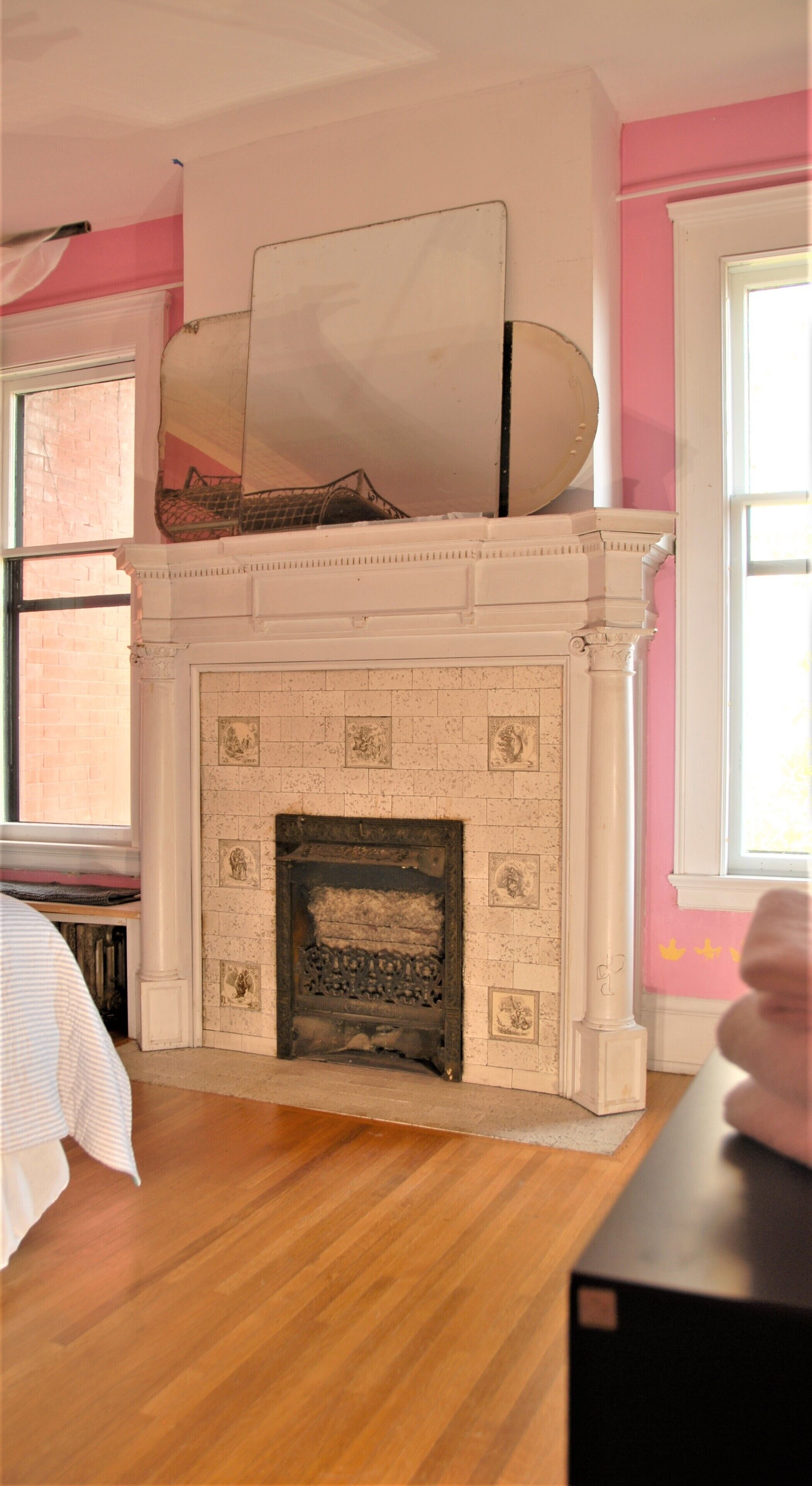 A room with a white fireplace, wooden flooring, and a pink wall.