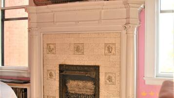 A room with a white fireplace, wooden flooring, and a pink wall.